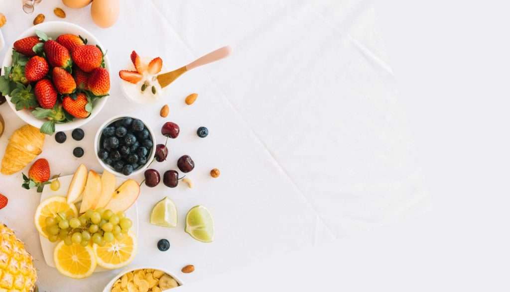 A vibrant arrangement of fresh fruits including sliced kiwi, oranges, strawberries, and blueberries, representing healthy nutrition for active aging.