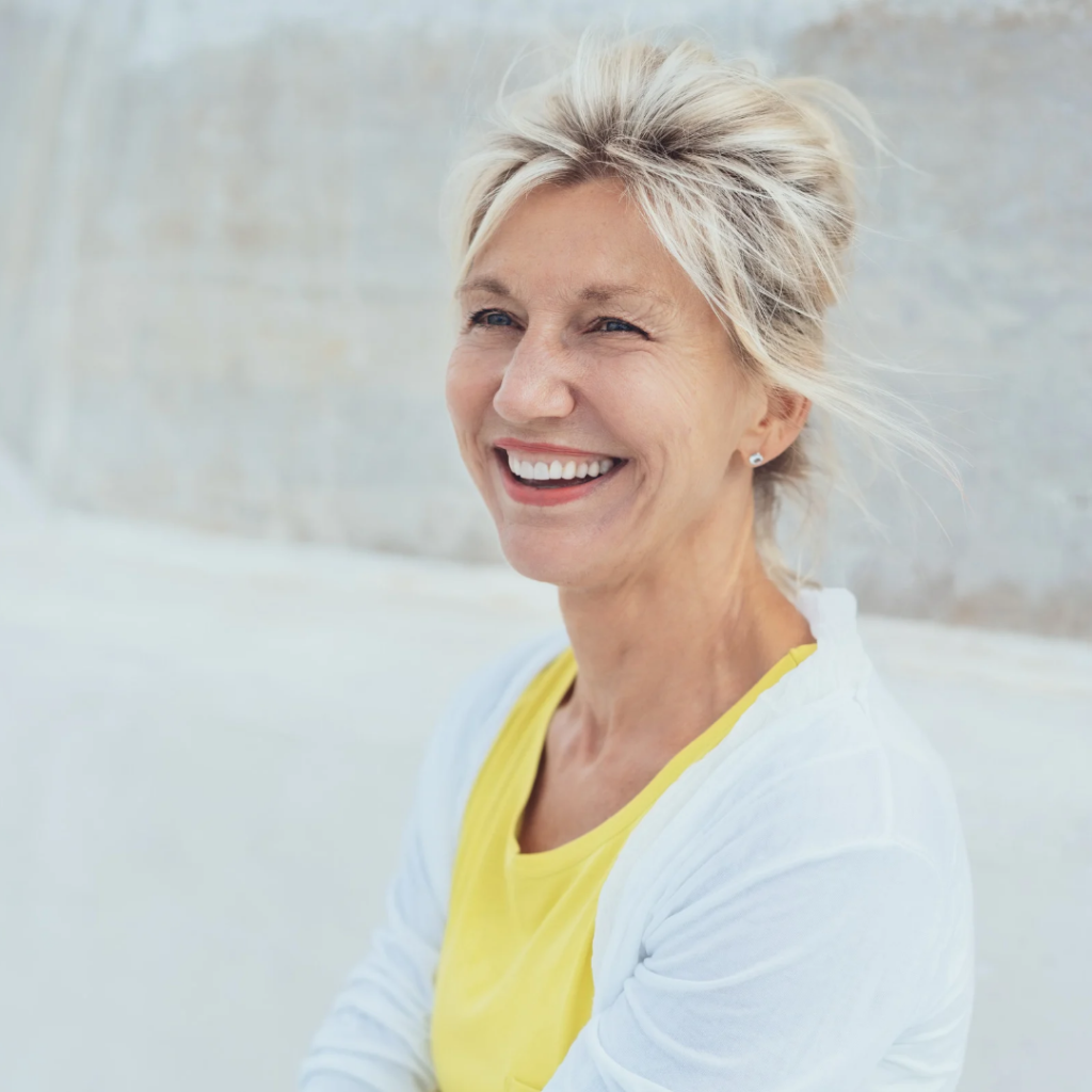 A smiling mature woman with short blonde hair looking forward, representing happiness, confidence, and vibrant healthy aging.