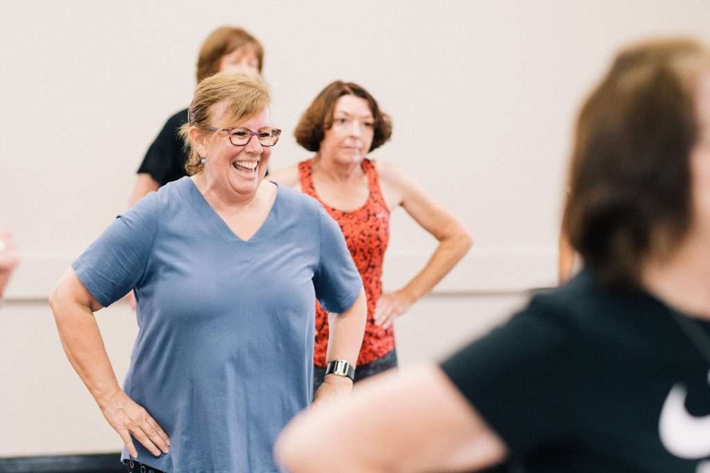 Active women smiling in a group fitness class, supporting each other in a consistent fitness routine.