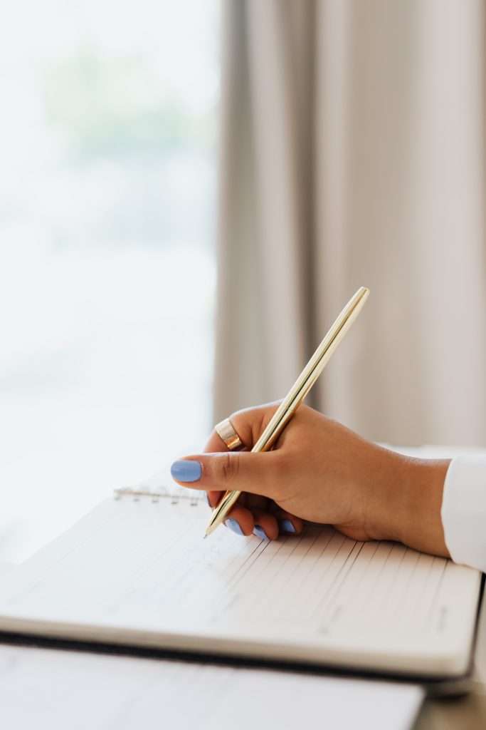 A close-up of a person writing in a daily journal to track their energy levels and maintain a consistent fitness routine.