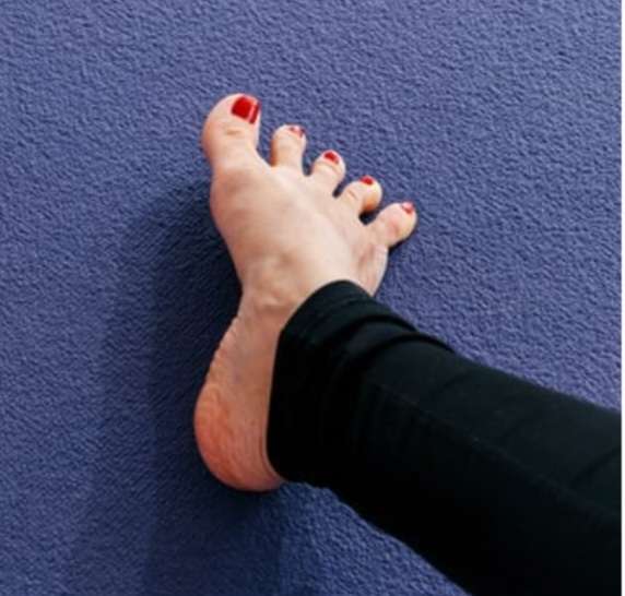 A close-up view of a bare foot resting on a dark surface, actively spreading the toes wide as part of a daily foot care routine to improve joint mobility and relieve tension.